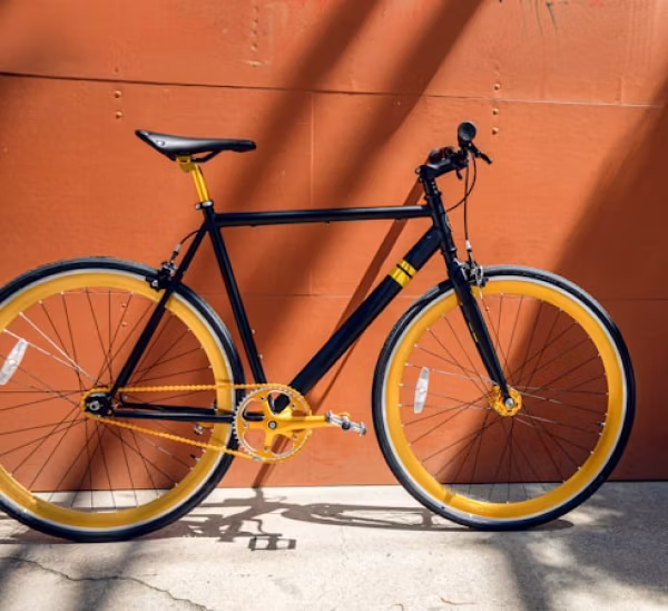 Black bicycle with bright yellow wheels, chain, and seat post against an orange wall.