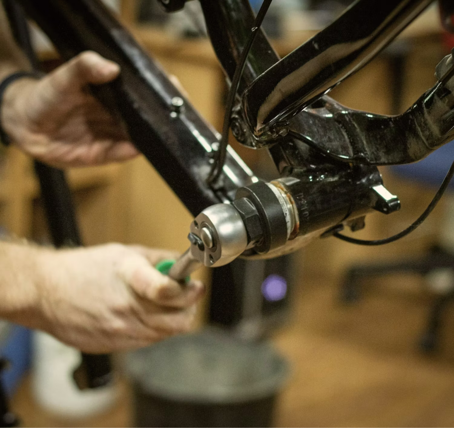Hands using a tool to adjust or repair a black bicycle frame component indoors.