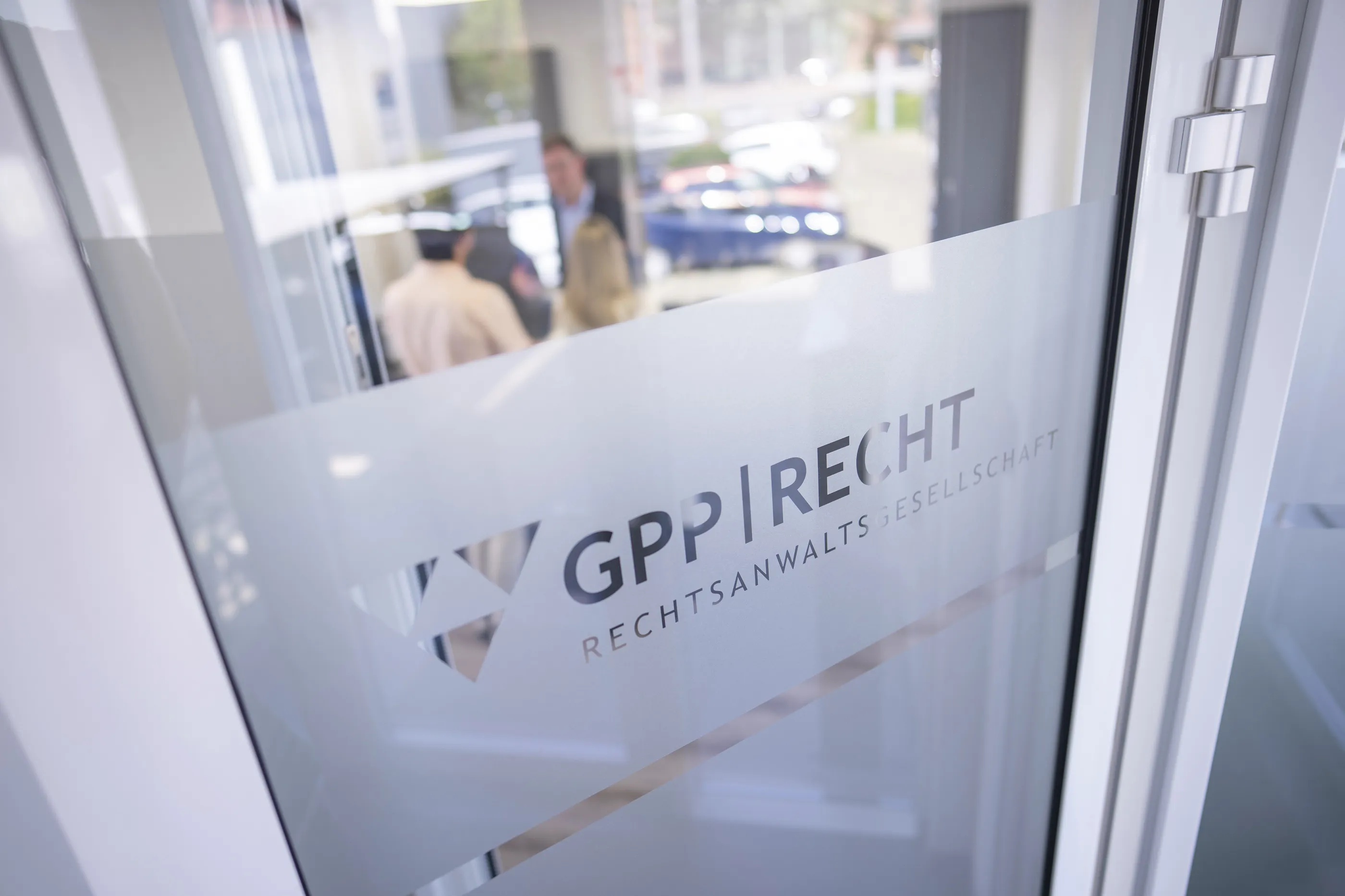 Glastür mit Logo von GPP Recht, Rechtsanwaltsgesellschaft, dahinter unscharfe Menschen im Gespräch.