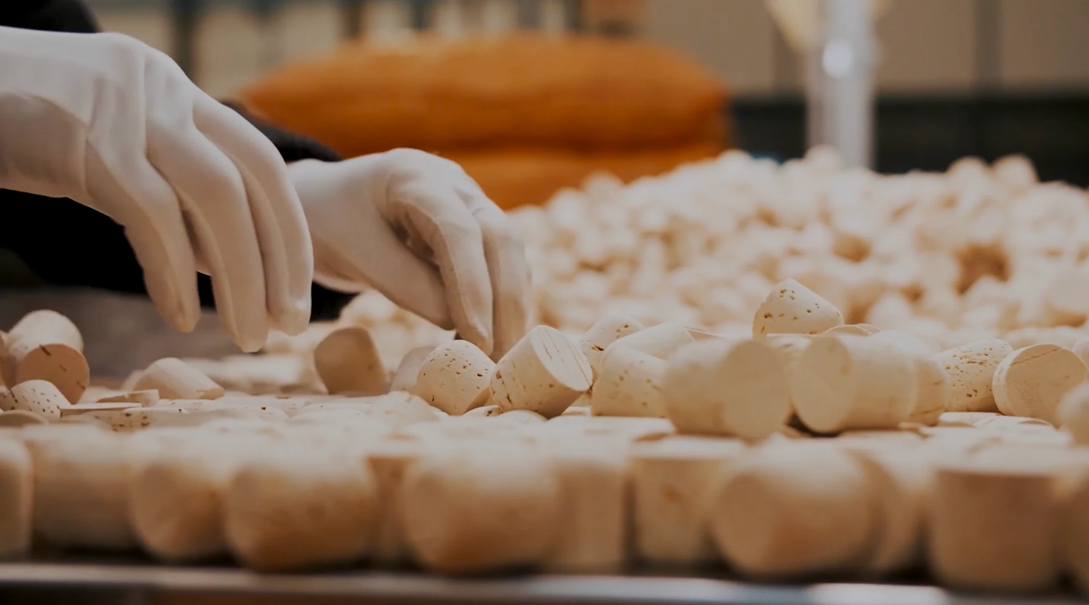 Two hands wearing white gloves sorting or inspecting many wine corks spread out on a surface