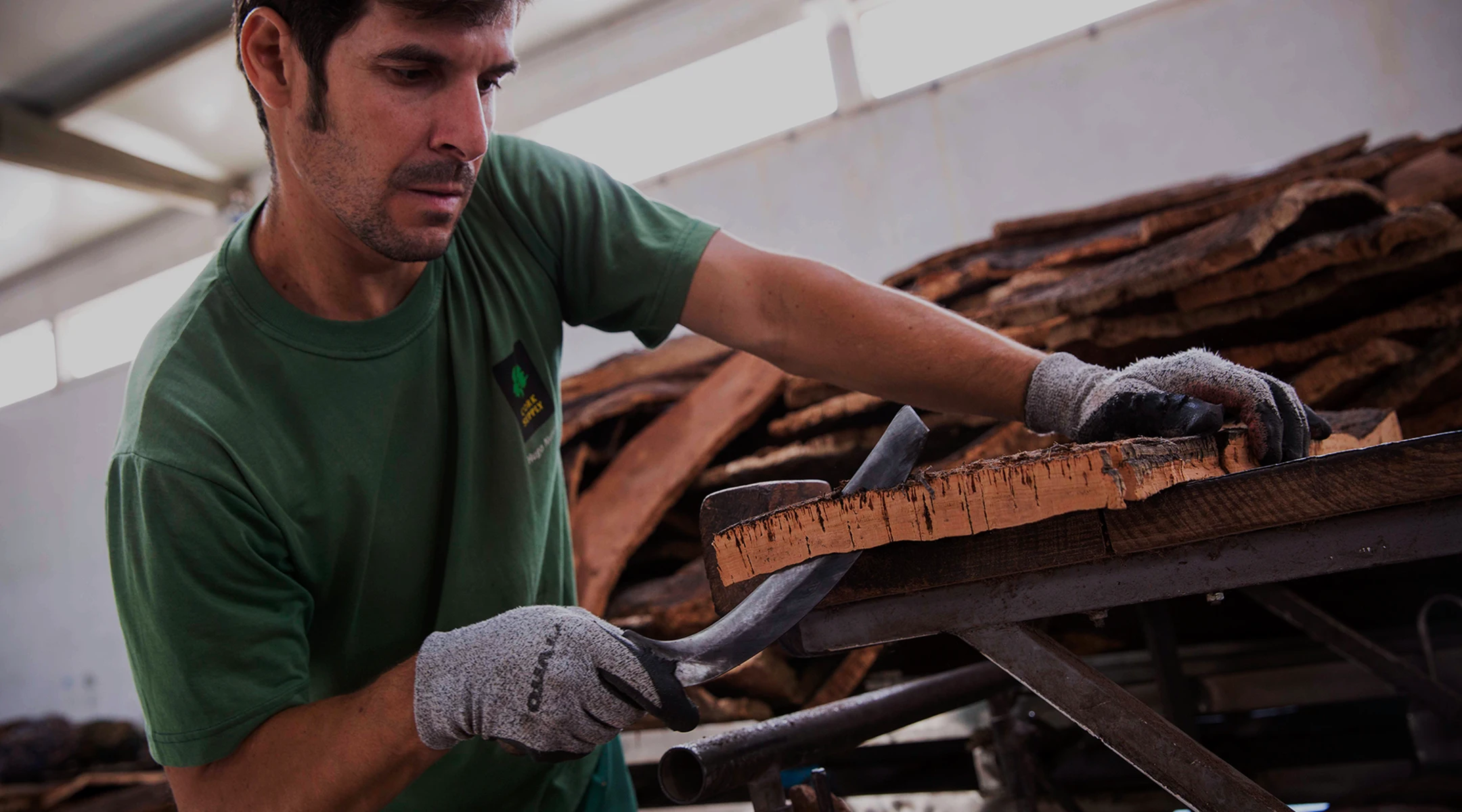 Man carefully trimming a piece of cork bark on a workbench inside a workshop.