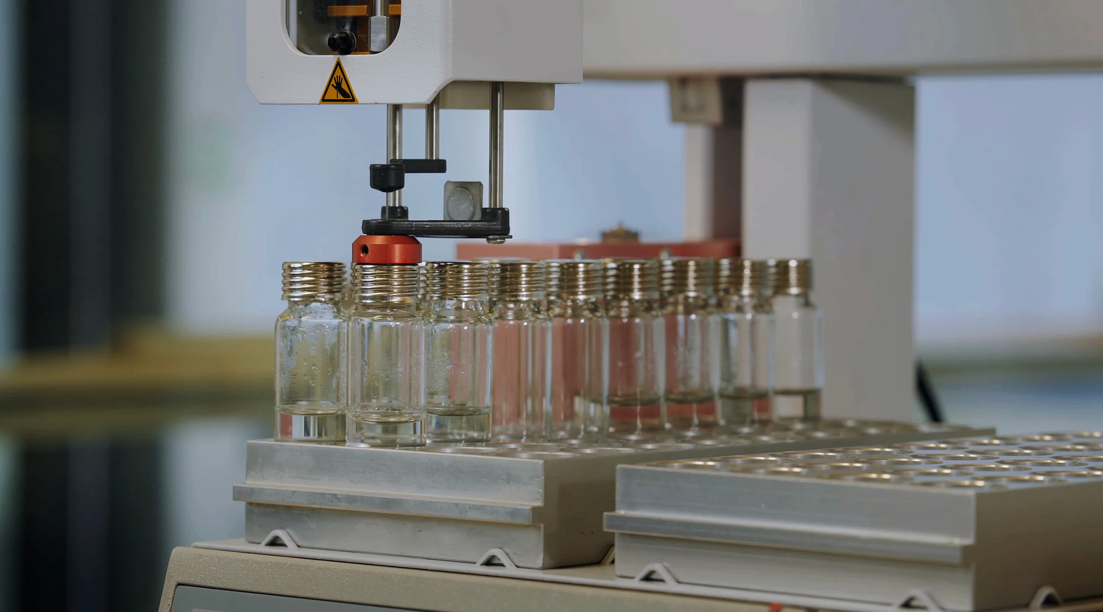 Several glass bottles lined up on a metal table with a person handling bottles in the background.