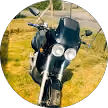 Moto noire avec phare allumé garée dans un champ herbeux sous un ciel clair.