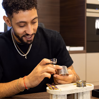 Un homme examine une bague avec une loupe au-dessus d'une table, entouré d'autres bijoux.