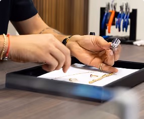 Person examining gold jewelry pieces on a tray in a workshop with pliers in the background.
