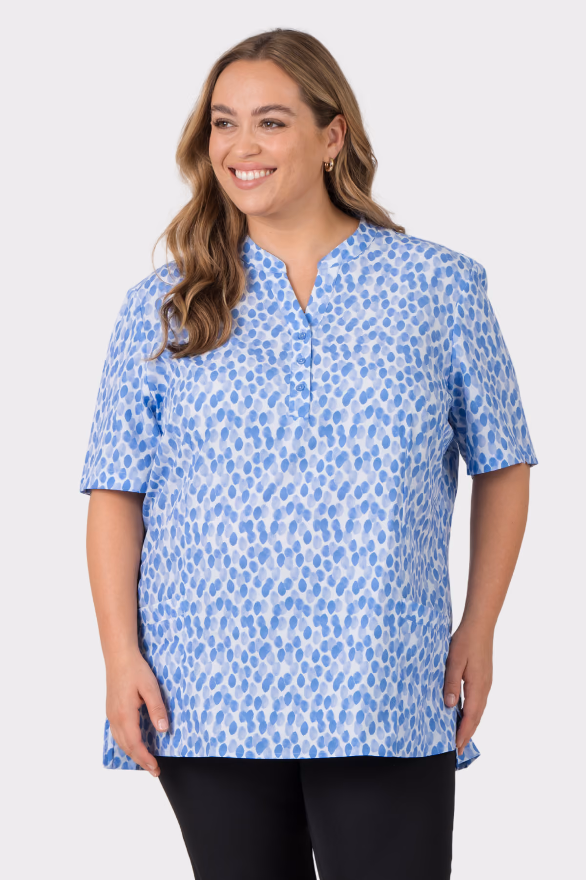 Woman wearing a blue patterned healthcare scrub top with black trousers