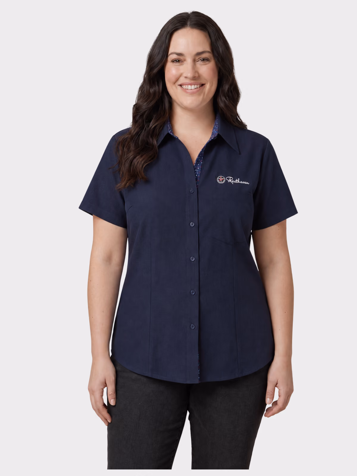 Woman wearing a navy short-sleeve aged care shirt with embroidered branding and dark trousers