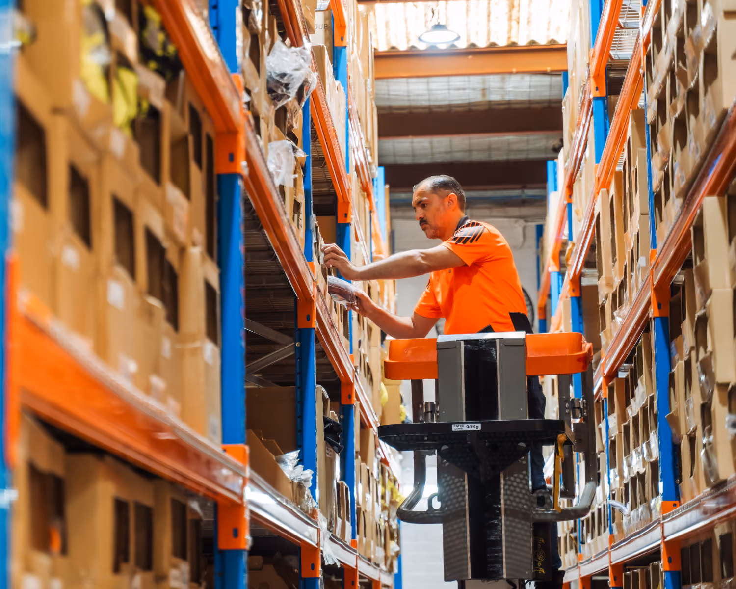 Warehouse worker on an order picker retrieving stock from high storage racking