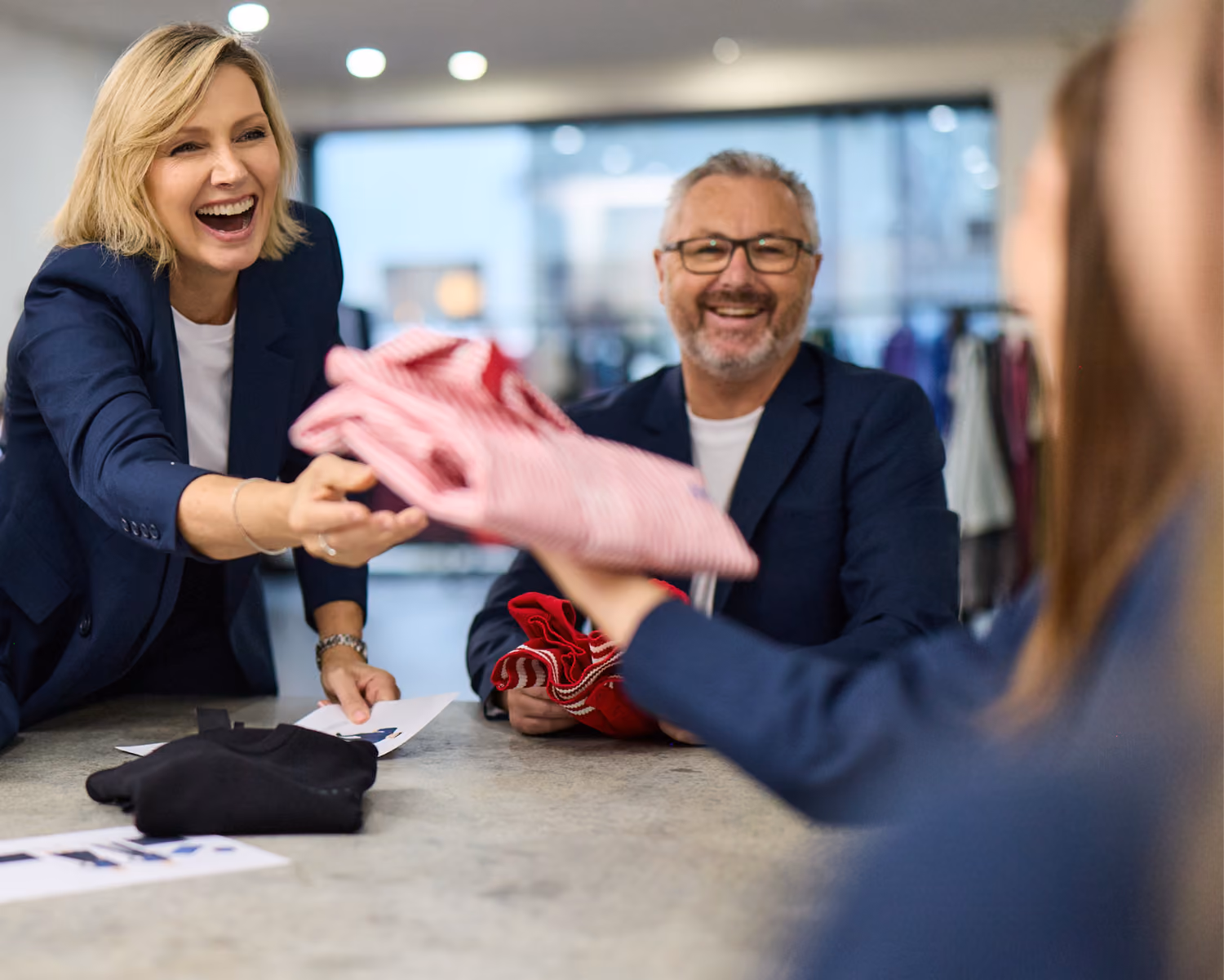 Total Image account manager handing a pink garment to smiling clients across a table