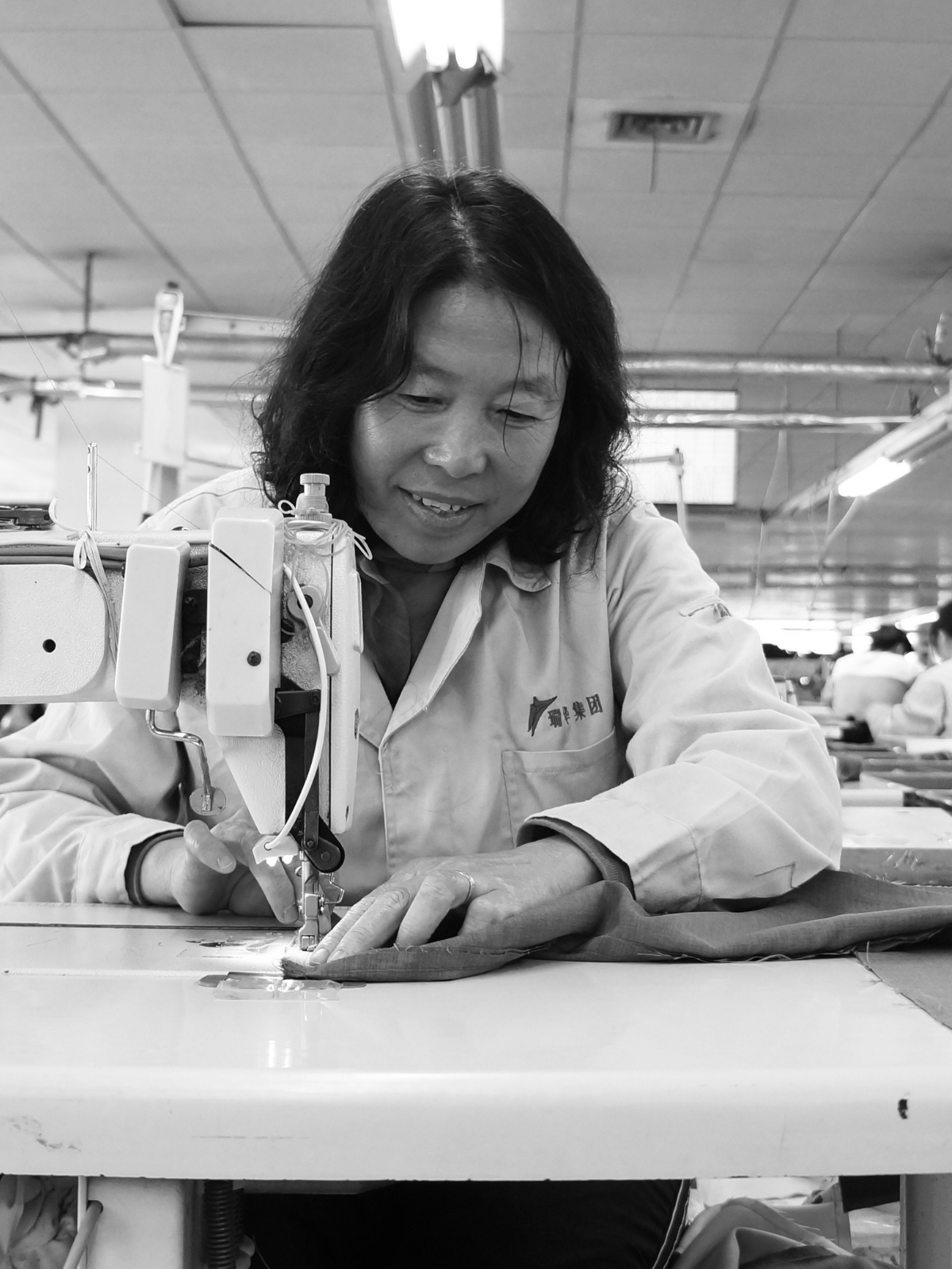 Garment worker smiling while sewing fabric at an industrial sewing machine