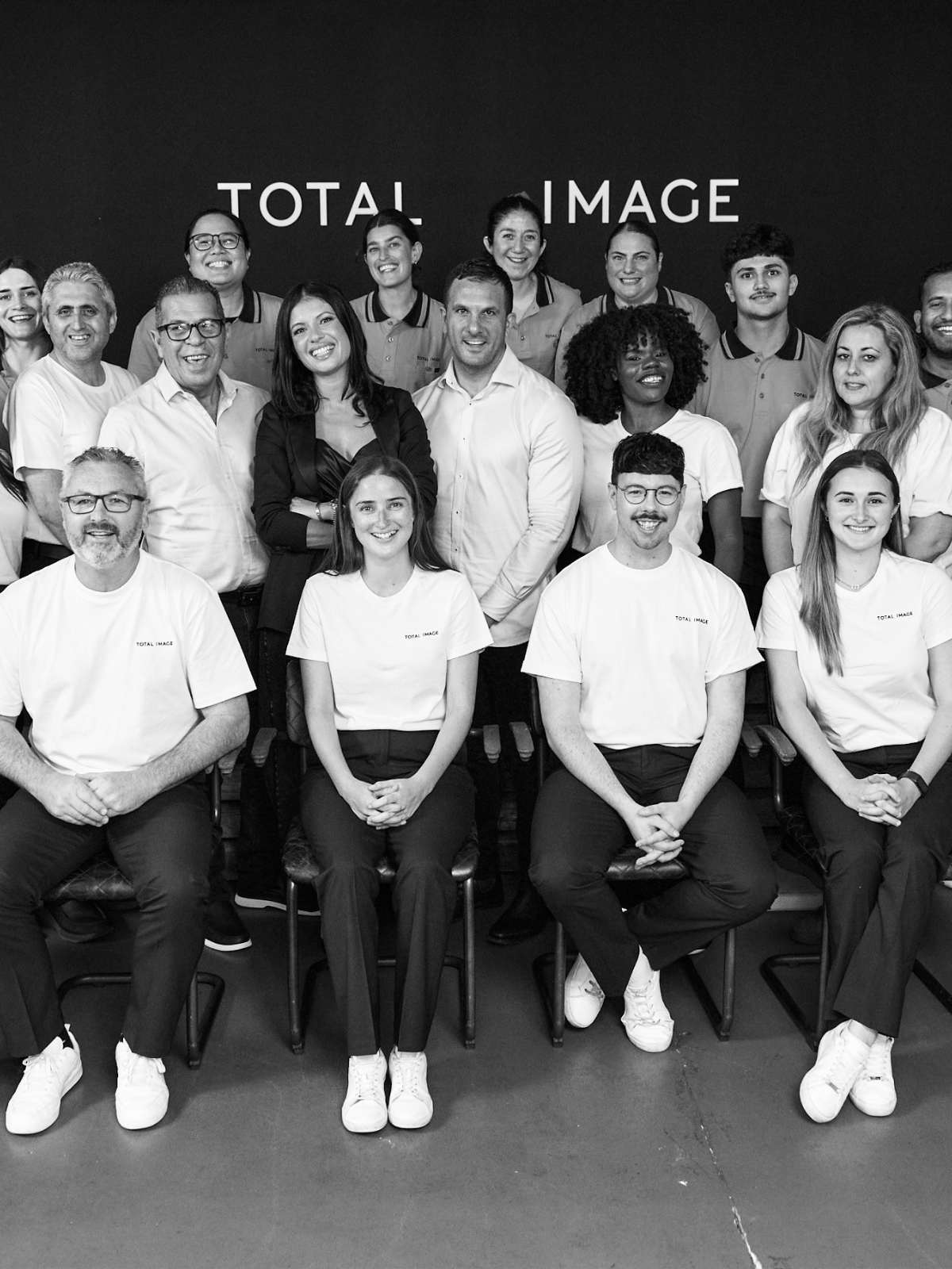 Total Image team group photo in front of the company logo wall