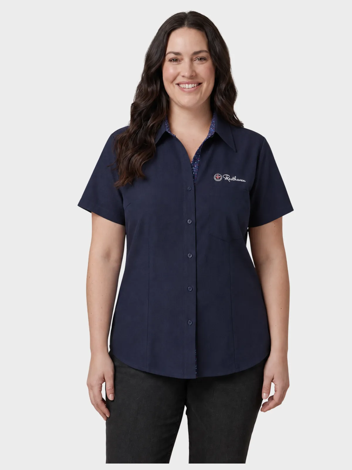 Woman wearing a navy short-sleeve aged care shirt with embroidered logo and dark trousers
