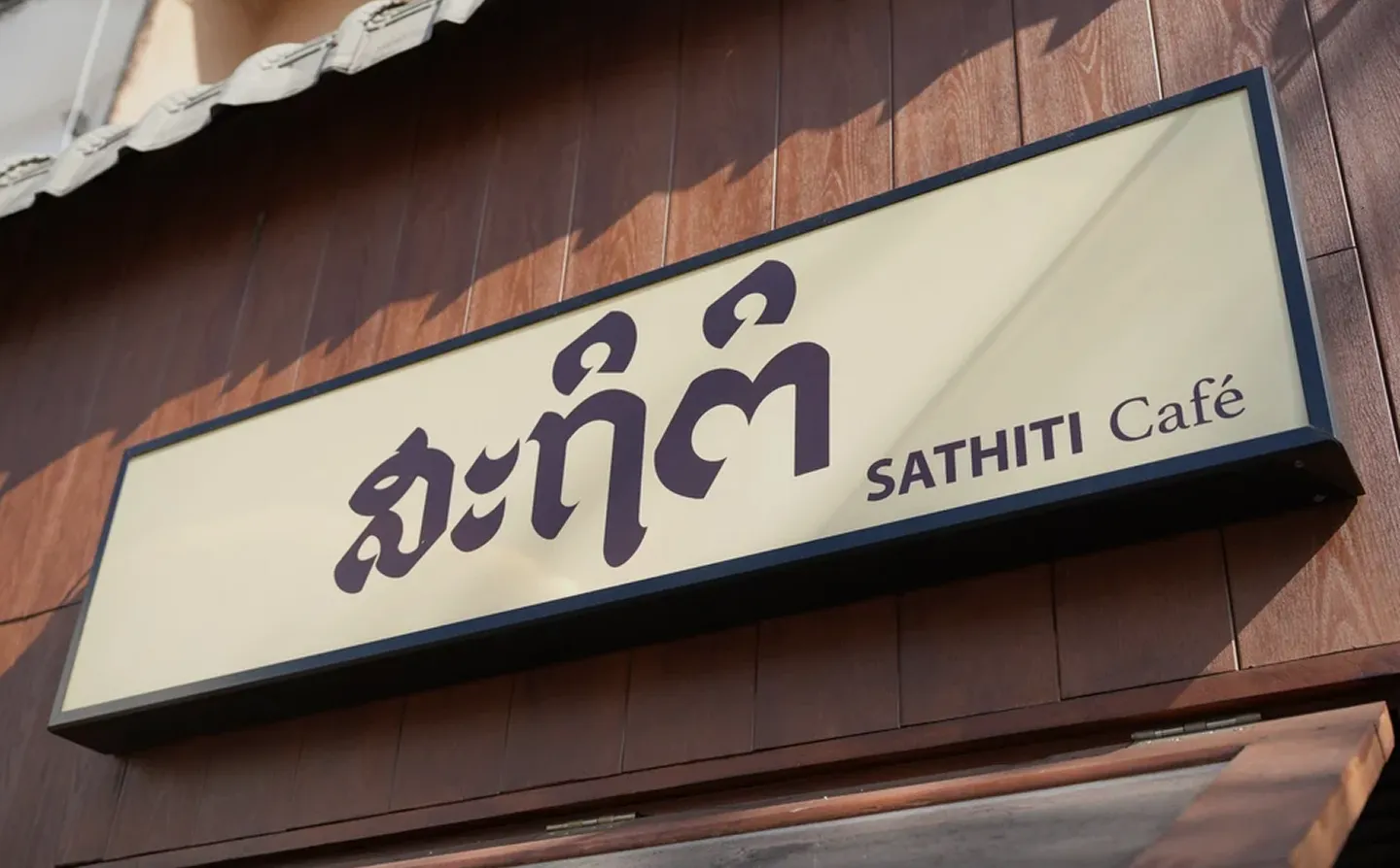 Outdoor sign for SATHITI Café mounted on a wooden wall under a tiled roof.