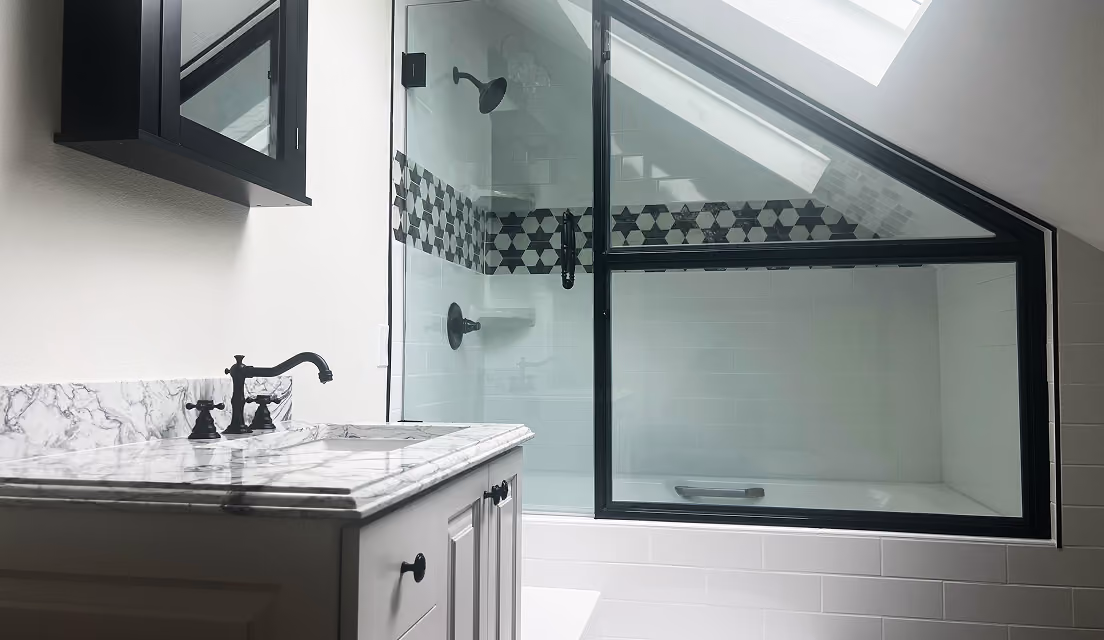 Modern bathroom with white marble sink, black fixtures, and glass shower with black geometric tiles.