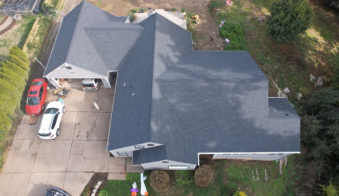 Aerial view of a house with a dark roof, driveway with cars, and a lawn with Halloween decorations.