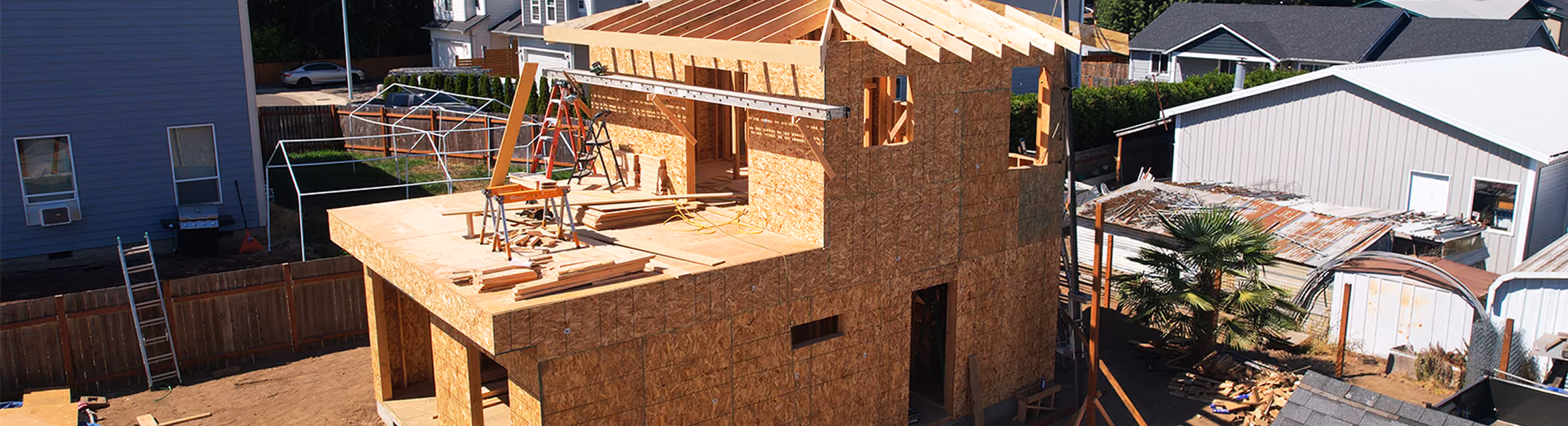New house under construction framed with oriented strand board sheathing and exposed roof trusses.