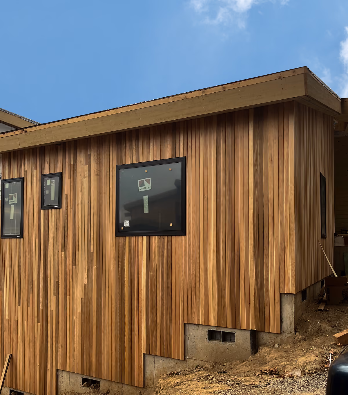 Exterior of a house under construction with vertical wooden siding and black framed windows.