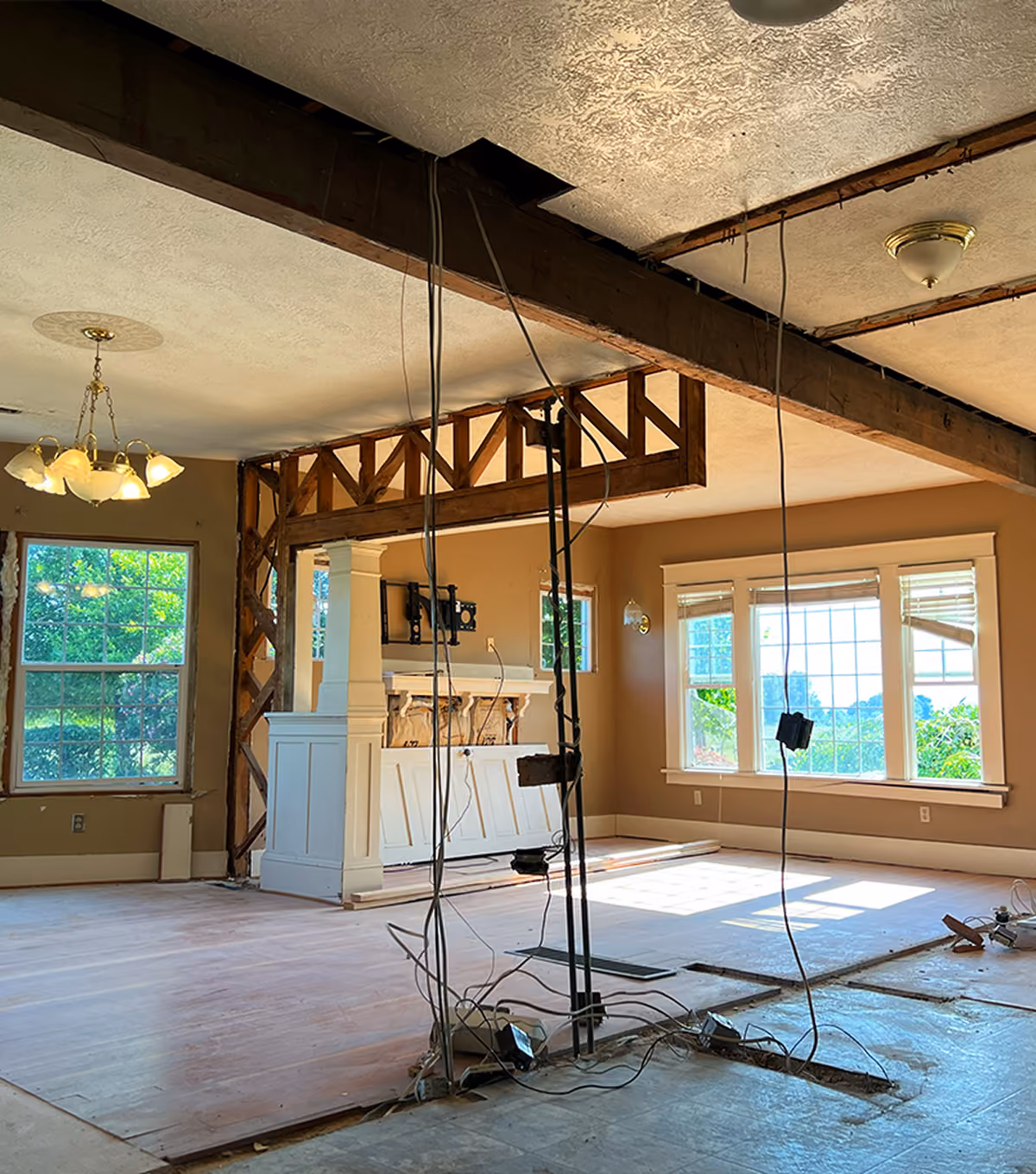 Interior view of a partially renovated room with exposed beams, wiring, and large windows.