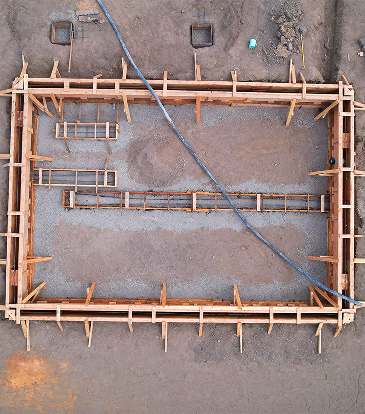 Aerial view of a rectangular construction site with wooden framing and gravel inside the foundation.