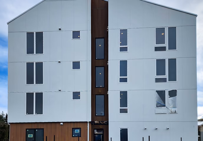 Modern building with white siding, multiple rectangular windows, and a brown vertical panel center.