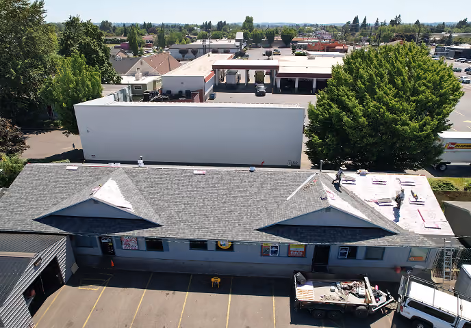 Aerial view of a building with workers installing roofing materials on one side of the roof.