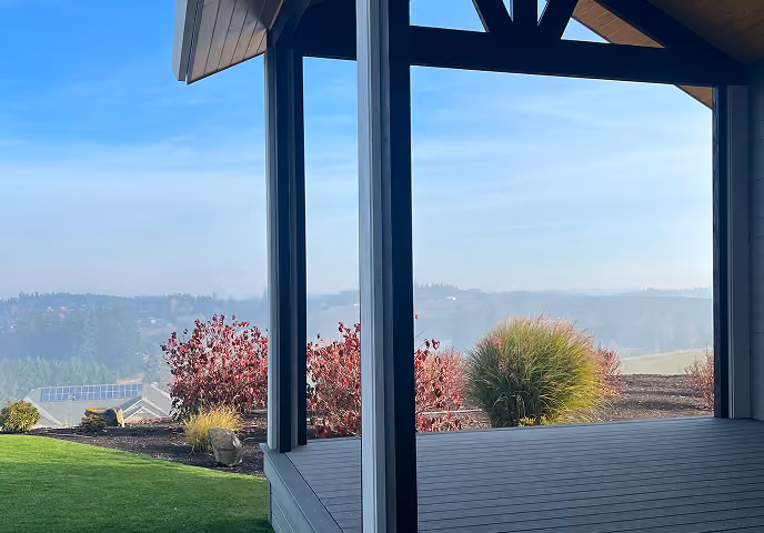 Covered deck with gray wood flooring overlooking a scenic hilly landscape under a clear sky.