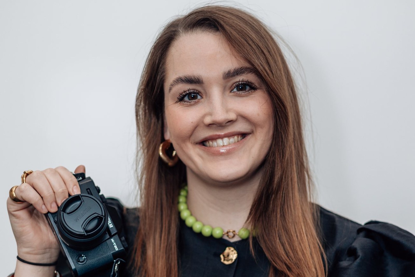 Lachende vrouw met systeemcamera in haar hand voor een lichte achtergrond