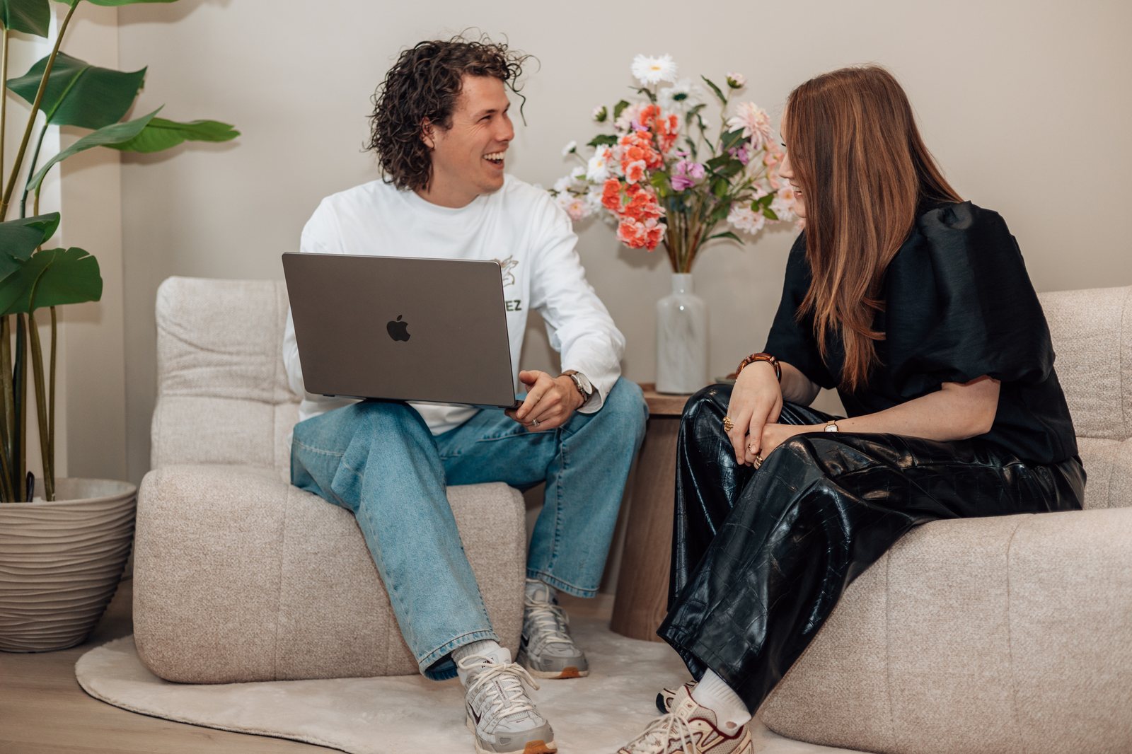 Twee collega's in gesprek op een bank, een van hen met een laptop op schoot