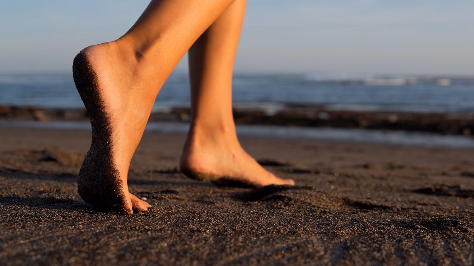 Bare feet walking on sand towards the sea