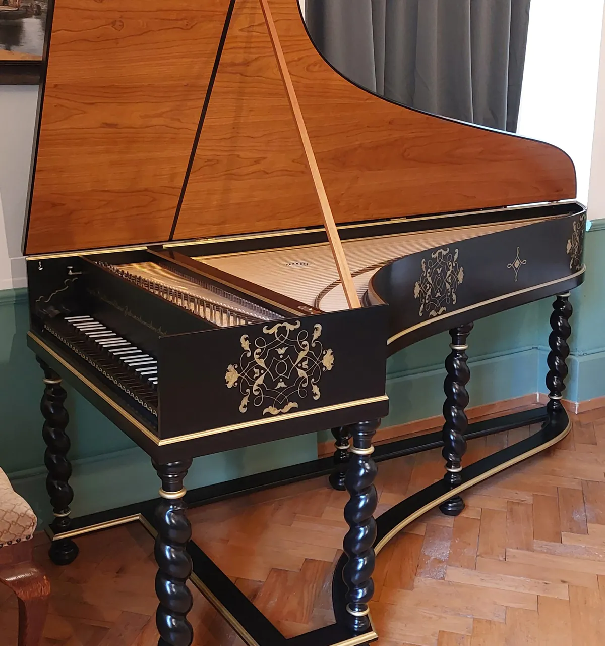 Antique wooden harpsichord with ornate gold decorations and twisted legs on a parquet floor.