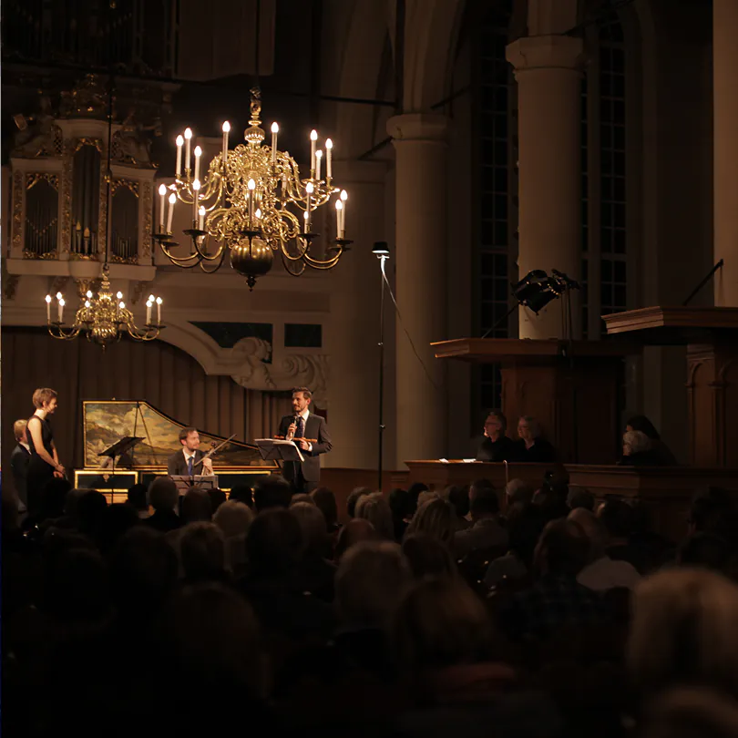 Musicians performing in a dimly lit ornate hall with chandeliers and audience watching.