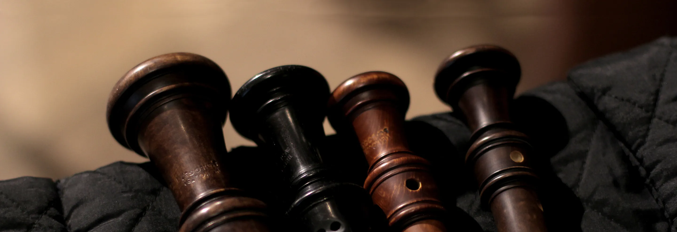 Close-up of four wooden recorders lying on a black quilted fabric.
