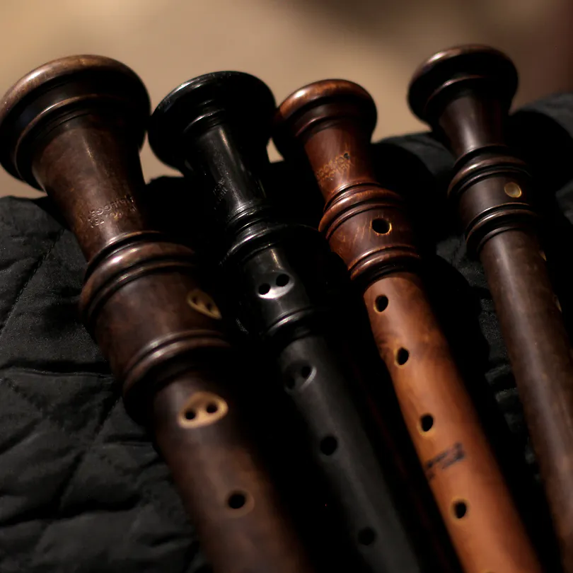 Four wooden recorders of different shades arranged side by side on a dark fabric background.