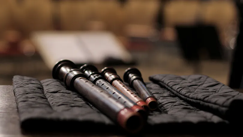 Four wooden recorders of varying sizes lying side by side on a black quilted cloth.