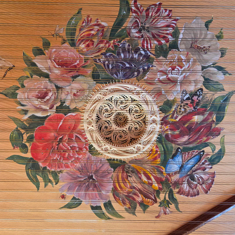 Close-up of a stringed instrument with a central carved rosette surrounded by colorful painted flowers and butterflies.