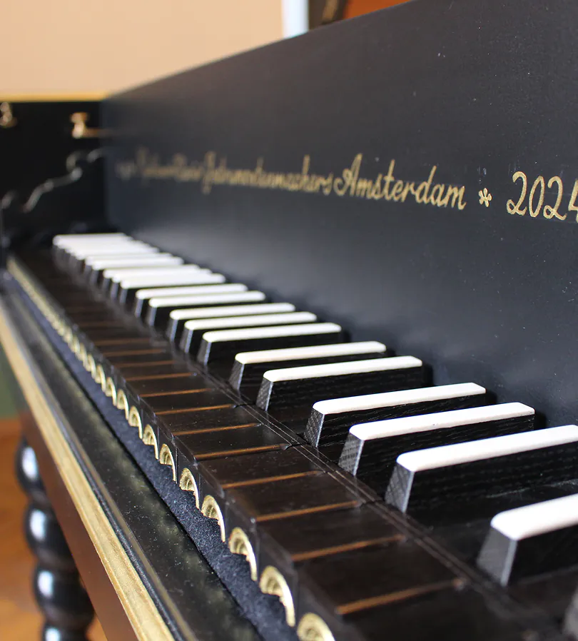 Close-up of a black harpsichord keyboard with white and black keys and gold lettering on the side.