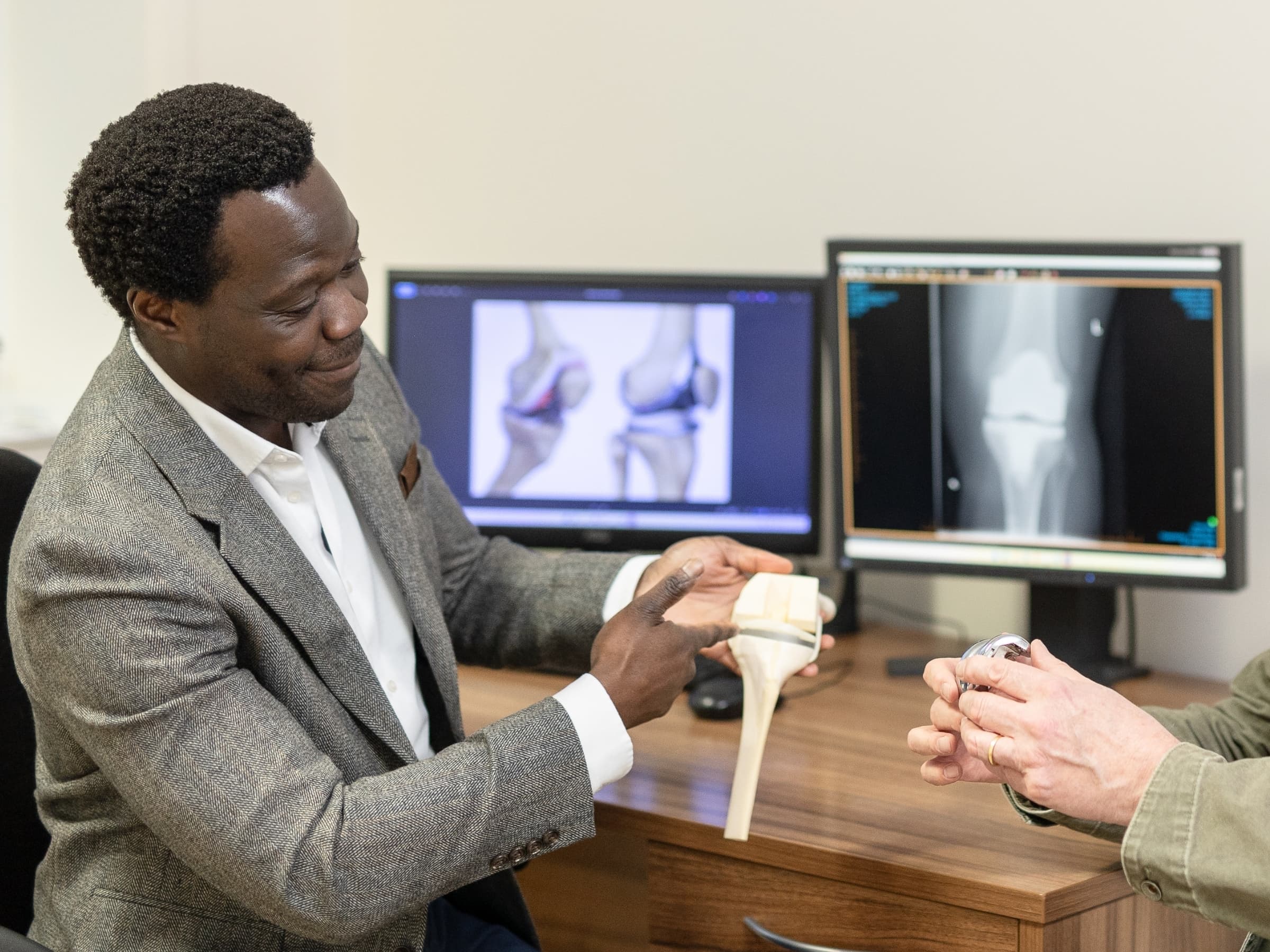 Mr Oni looking at a knee model while at his desk and pointing to a particular area on the model. 