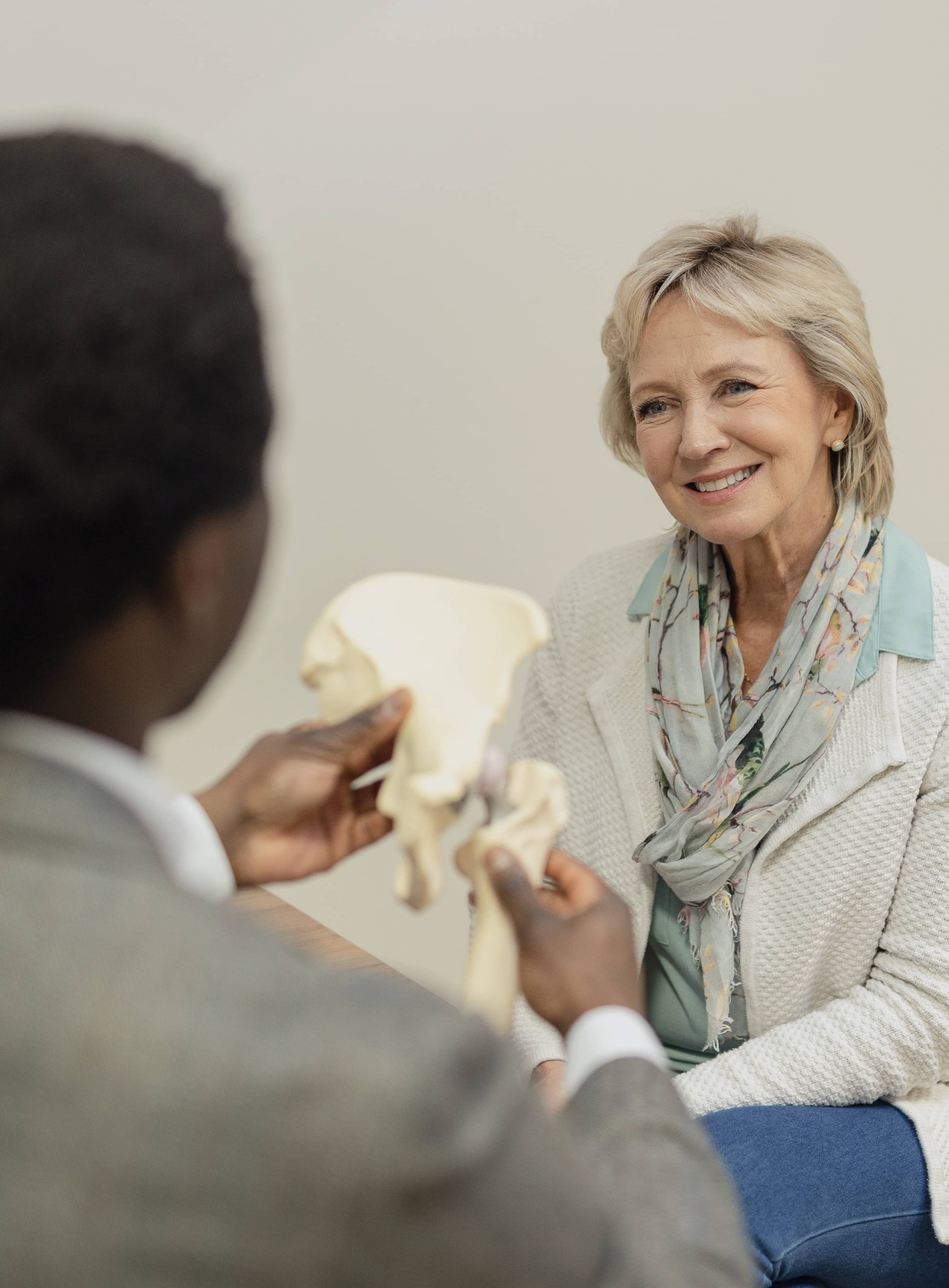 Mr Oni with his back to the camera showing a female patient a model of a hip joint while she is smiling and looking back at him. 