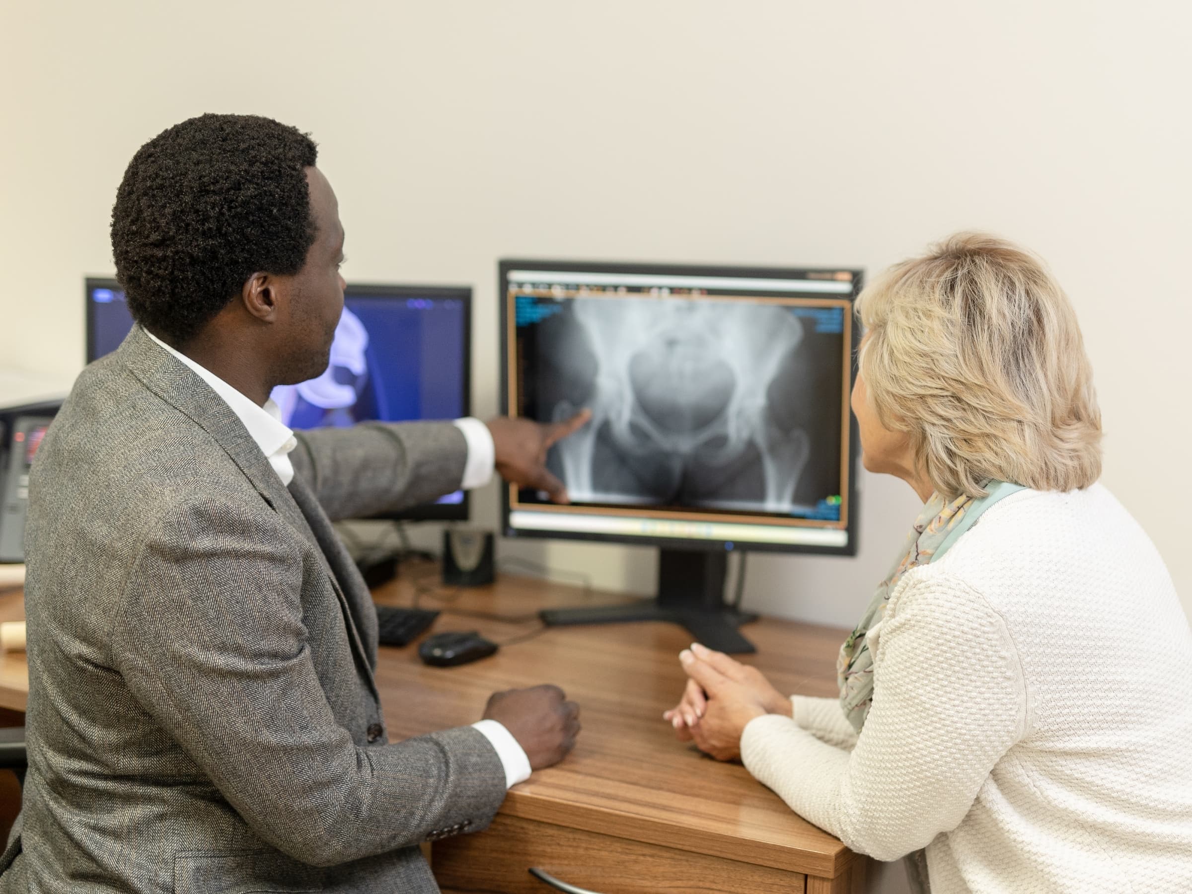 Mr Oni explaining hip bursitis to an older looking female patient at his desk.