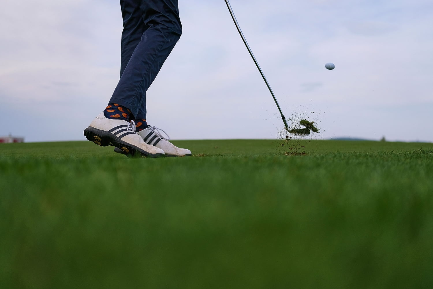 the legs of golfer with club and ball that has just been hit