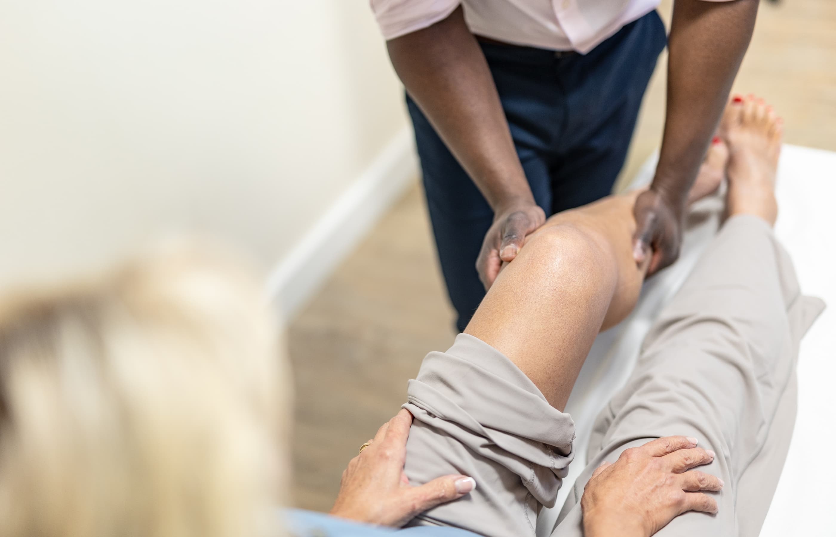 Mr oni examining the knee of an older female patient laying on an examination table in the surgeons consulting room