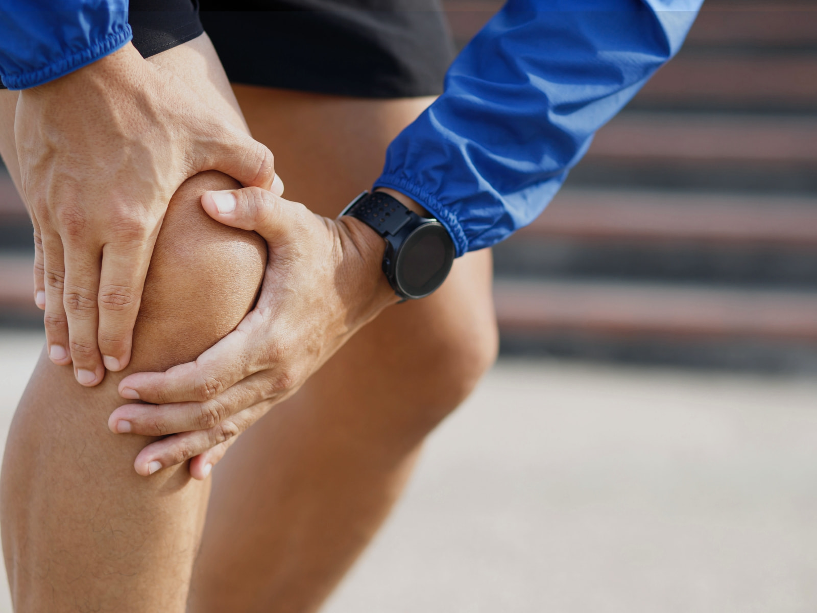 a male runner bent over clutching his knee cap in pain