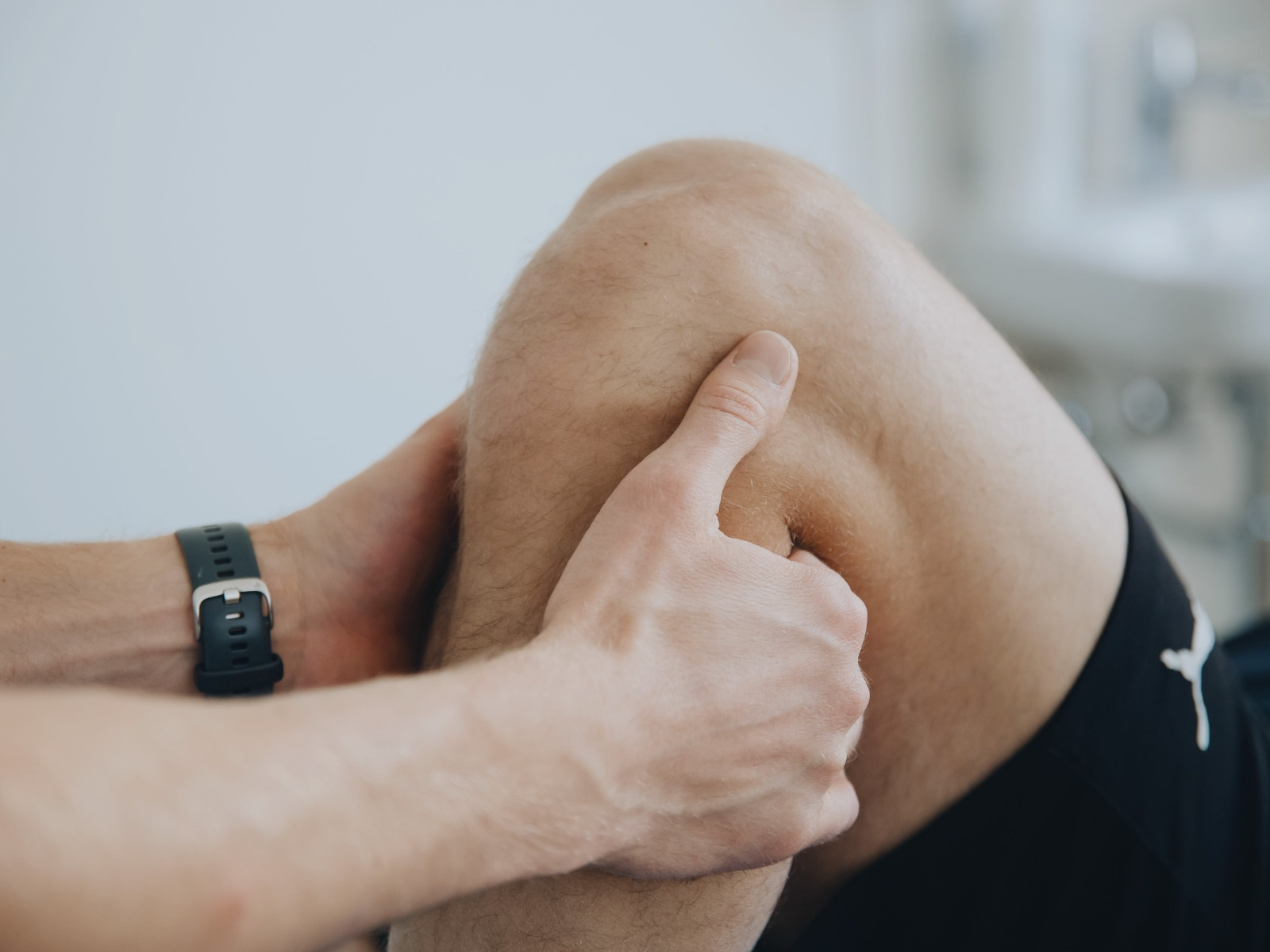 A physio's hands manipulating the knee of male patient in running shorts
