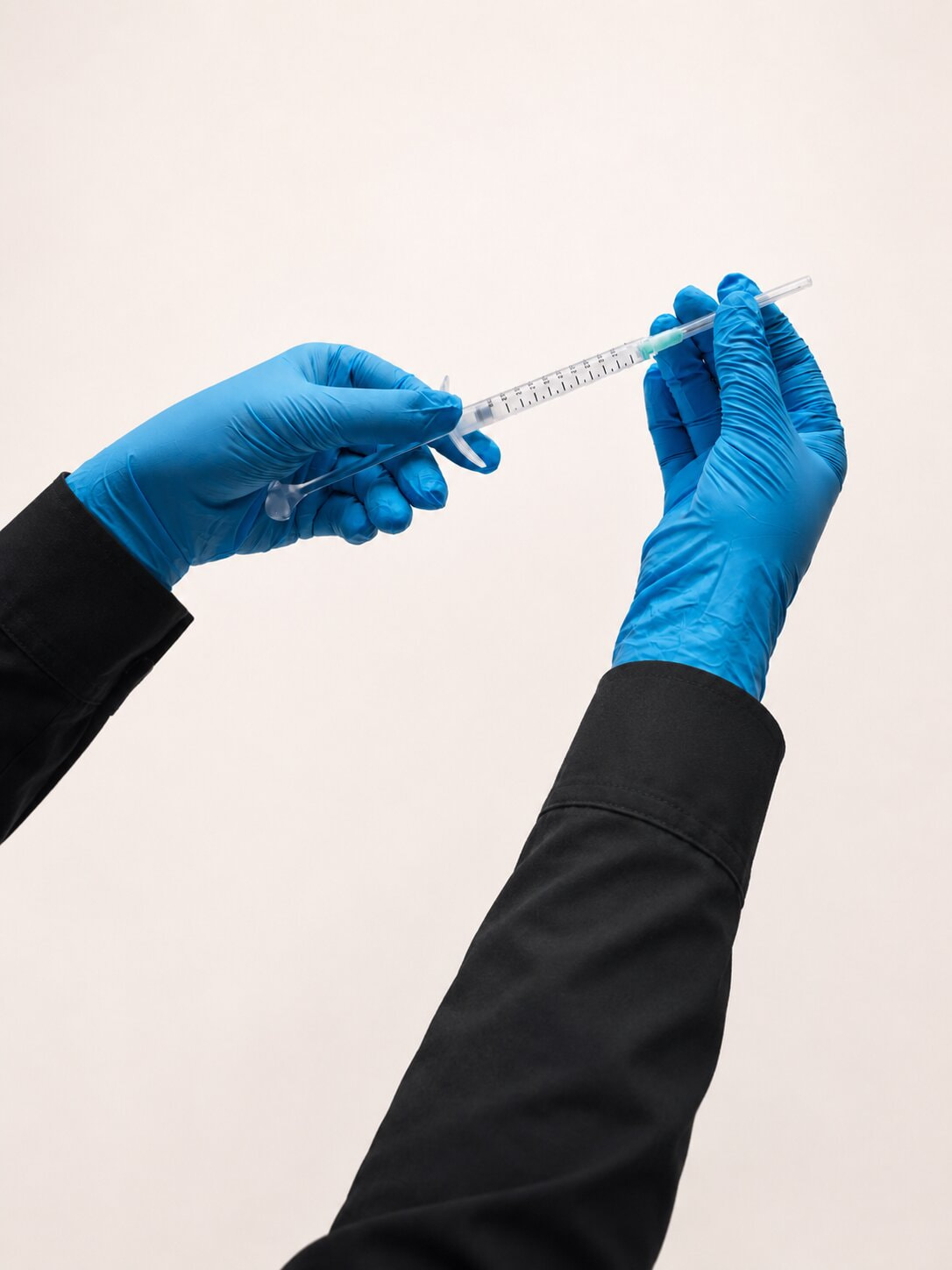 Hands blue glove with black sleeves, holding an arthrosamid injection needle in both hands.