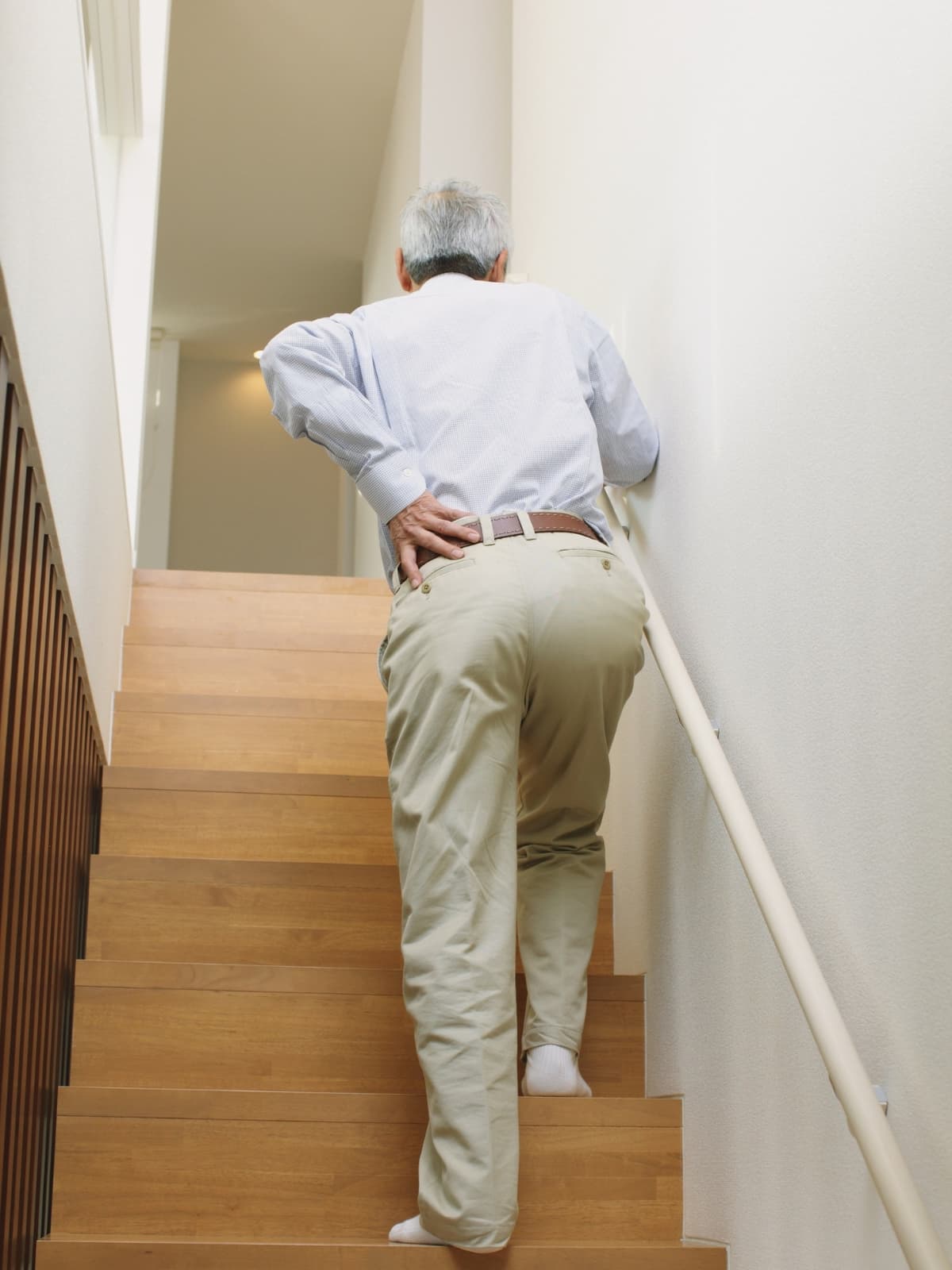 	an elderly person climbing the stairs clutching their lower back in pain