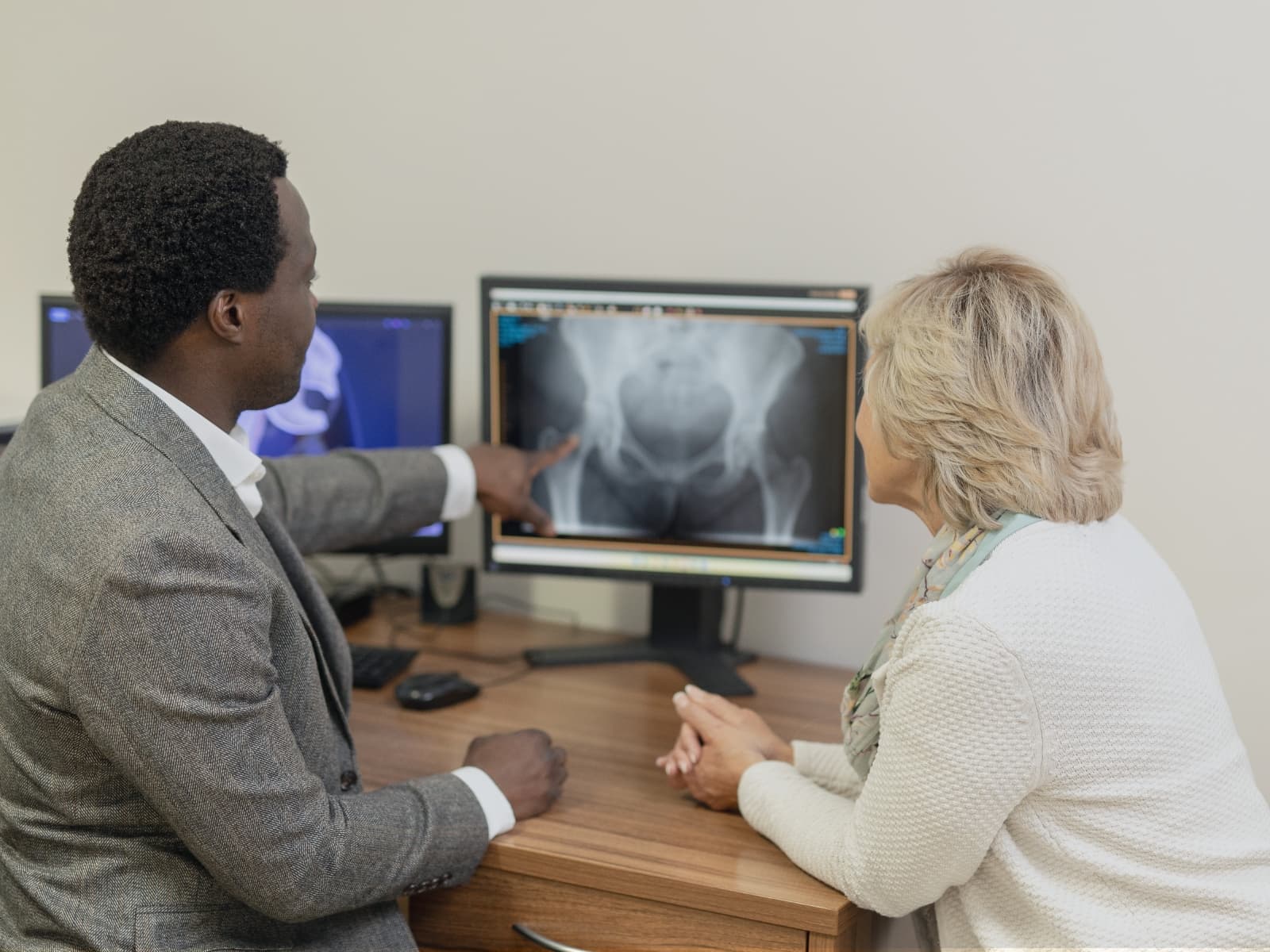 Mr oni explaining the hip model and replacement procedure to a female patient. they are sitting at his desk during a consultation.
