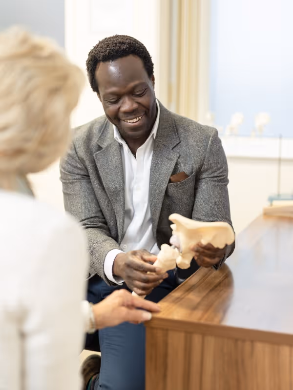 Mr oni looking at a model of a hip and explaining it to the female patient sitting opposite him