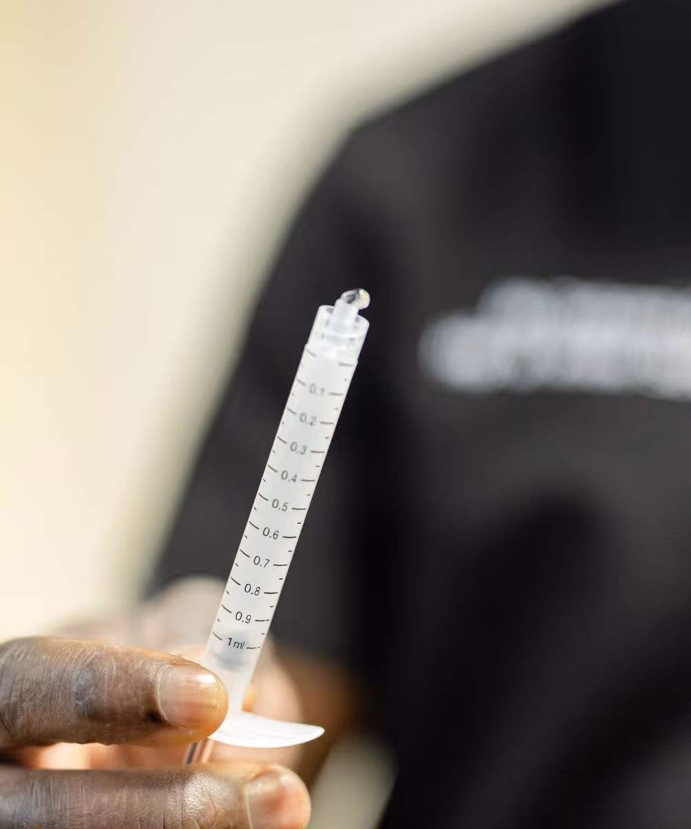 Mr Oni holding up a syringe without a needle containing arthrosamid hydrogel. He is wearing black scrubs and is blurred in the background of the image