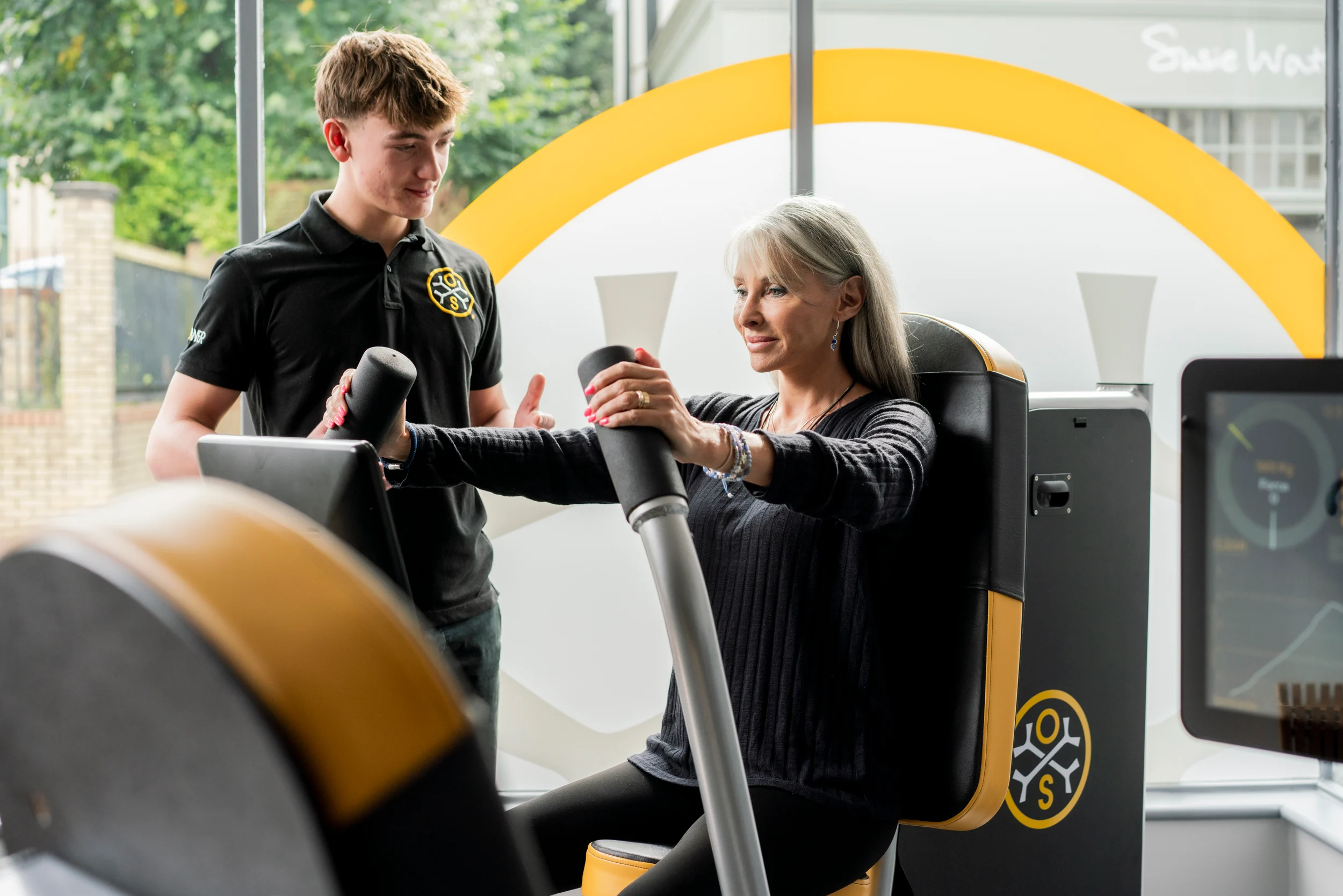 A woman using osteostrong gym equipment with a physio standing next to her in the osteostrong uniform.