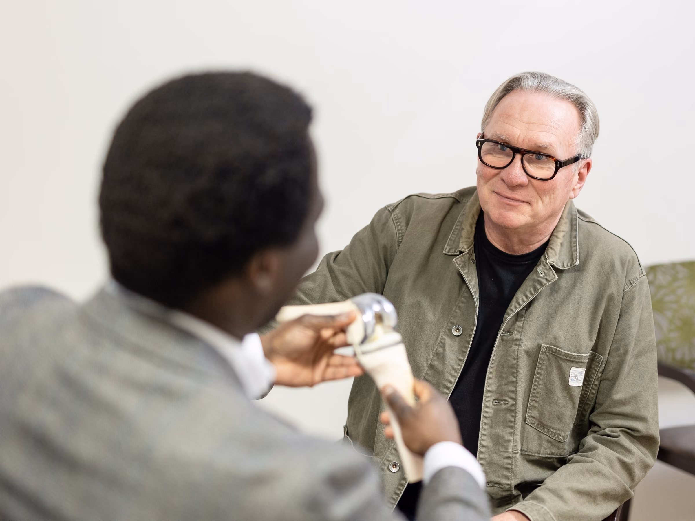 Mr Oni showing an anatomical knee joint model to a seated older man wearing glasses and a green jacket.
